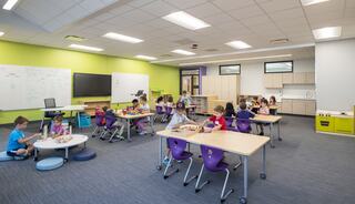 A vibrant classroom filled with children engaging in hands-on activities at tables, with colorful walls and interactive learning spaces.