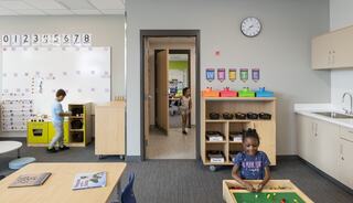 A vibrant classroom features children engaging in play, colorful storage units, and educational materials, promoting a fun learning environment.