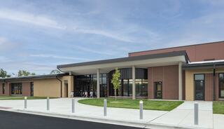 A modern building features a spacious entrance, large windows, and landscaped surroundings, showcasing a welcoming architectural design.