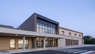 A modern building features large glass windows, a sleek design, and a welcoming entrance, set against a clear evening sky.