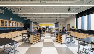 A spacious classroom with lab stations and large windows, featuring students engaged in hands-on activities amidst modern design elements.