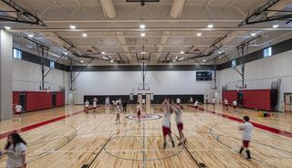 A spacious gymnasium filled with students in white shirts and red shorts engaging in various basketball activities and drills.