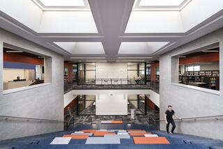 A modern, spacious interior features open areas, large windows, and a multi-level staircase, connecting a library and study spaces.