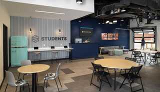 Austin Stone South student's lounge designed by FGM Architects featuring a retro teal refrigerator, patterned wall design, bold artwork, lounge, tables and a garage door access to the outdoors.