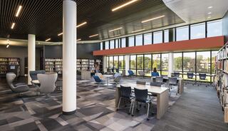 A modern library featuring spacious seating areas, large windows, and bookshelves, creating a bright and inviting atmosphere for reading and study.