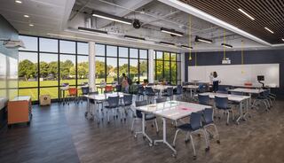 A modern classroom features flexible furniture, bright windows, and views of green outdoor space, fostering a collaborative learning environment.
