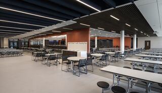 A modern, spacious cafeteria with tables and chairs arranged neatly, featuring large windows and clean lines in an inviting atmosphere.