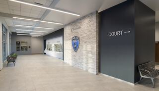 A modern hallway features a police badge on a stone wall and directional signage for the court, with benches along the sides.