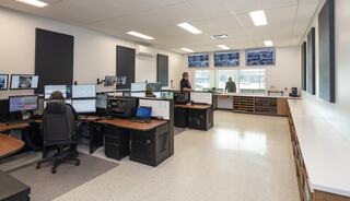 A modern control room featuring multiple computer stations, displays showing information, and personnel engaged in various tasks.