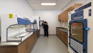 A room with modern lab equipment, including safety cabinets. An officer stands by, inspecting one of the cabinets.