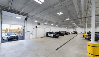 A spacious garage with multiple police vehicles parked inside, featuring bright lighting and a large open bay door.