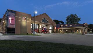 A modern fire station features large garage doors and a welcoming entrance, set against a dusk sky with well-maintained landscaping.