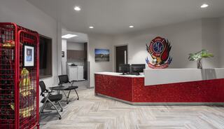 A modern reception area with a red glittery desk, seating, a framed photo, and a firefighter suit display, exuding a welcoming atmosphere.