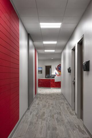 A well-lit corridor with red accent walls, leading to a reception area featuring colorful artwork and modern design elements.