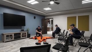 Firefighters in a training room engage with emergency gear, preparing for a discussion. The setting features modern decor and seating.