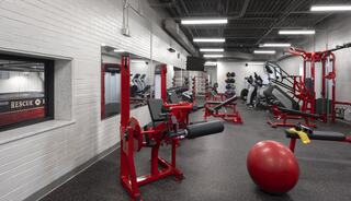 A modern gym featuring various exercise equipment, including weights and cardio machines, with a vibrant red and black color scheme.