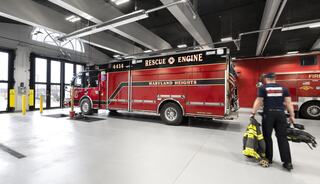 A red rescue engine marked "Maryland Heights" is parked inside a fire station, with a firefighter preparing equipment nearby.