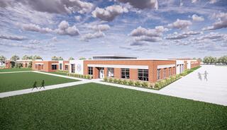 A modern educational building features red brick and large windows, surrounded by green lawns and pathways, under a cloudy blue sky.
