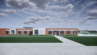 A modern brick building with a manicured lawn and cloudy blue sky, featuring a clearly marked entrance and a pathway leading towards it.