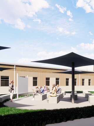 A sunny outdoor meeting space features shaded areas with seating, where a group listens to a speaker amid lush greenery.