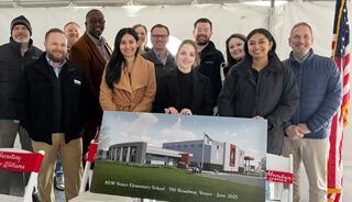 A group of individuals stands together, smiling, in front of a rendering of the new Venice Elementary School, showcasing the upcoming project.