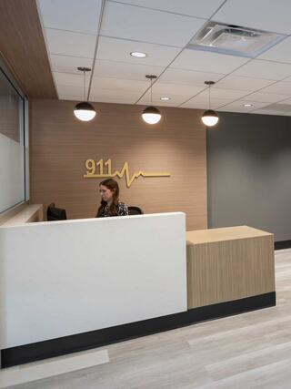 A modern reception area with a 911 emblem, featuring warm wood tones, a sleek desk, and a staff member at the phone.