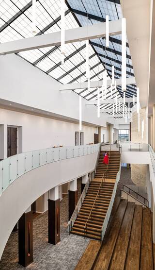 A contemporary interior space features a grand staircase, modern light fixtures, and large windows letting in natural light.