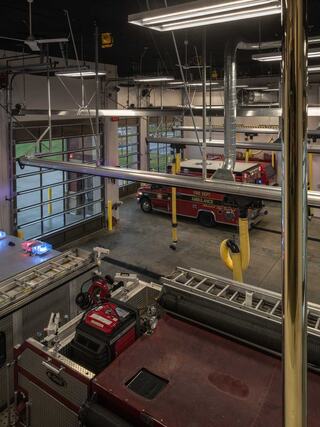 A spacious fire station featuring emergency vehicles, a ladder, and bright lighting, with multiple garage doors for quick exits.