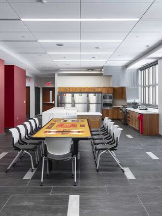 A modern kitchen features sleek cabinets, stainless appliances, and a large table surrounded by chairs, all in a spacious, well-lit area.