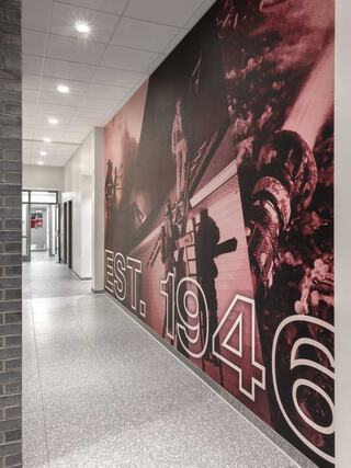 A hallway features a large mural emphasizing "EST. 1946," depicting scenes of action and history in vibrant colors.