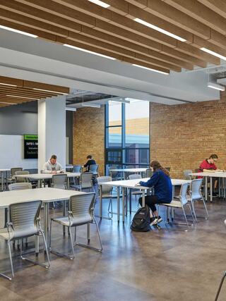 A spacious, modern study area features several students focused on their work at minimalist tables under a bright, welcoming atmosphere.