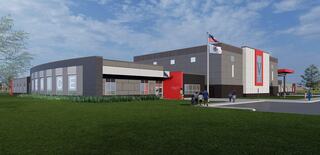 A modern building with a mix of gray and red elements, featuring large windows and an American flag, surrounded by green grass.