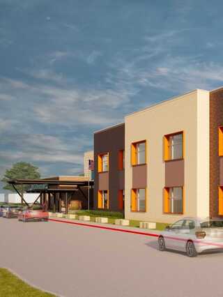 A modern building features a welcoming entrance, colorful window accents, and a landscaped front, set against a cloudy sky.