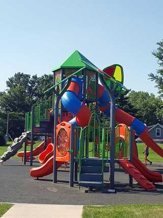 A colorful playground features slides, climbing structures, and a playscape under a clear blue sky, perfect for children's outdoor fun.