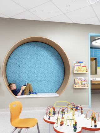 A cozy play area features a round nook with a blue wall, where a child sits reading. Nearby, shelves hold books, and a play table awaits engagement.