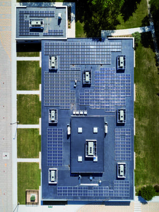 A flat roof covered with numerous solar panels, featuring air conditioning units, surrounded by green lawn and pathways.
