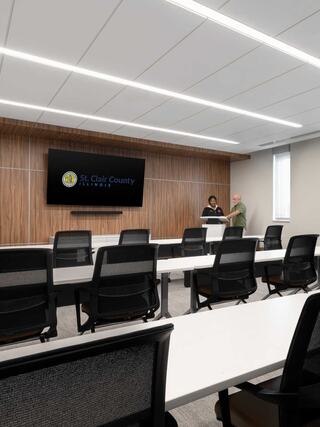 A modern conference room features rows of chairs, a sleek presentation screen, and two people engaging at the front near a wooden backdrop.