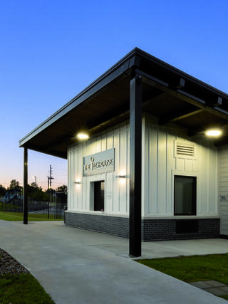 A modern, single-story building with a sleek design, featuring a welcoming entrance and outdoor path, set against a twilight sky.