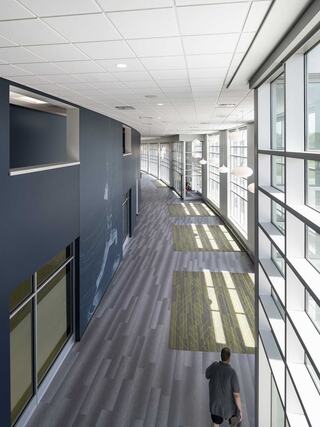 A modern corridor features large windows, sleek flooring, and a person walking, creating a bright and spacious atmosphere.