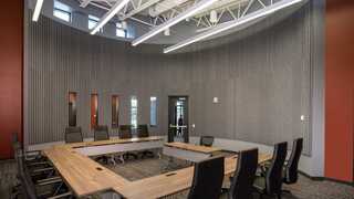 A modern conference room features a long table surrounded by ergonomic chairs, with large windows and textured walls creating a professional atmosphere.