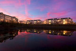 A serene dusk scene showcases apartments beside a calm pond, reflecting colorful twilight skies and warm lights glowing from the buildings.