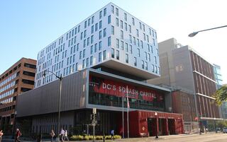 A modern architectural structure features a unique design, with prominent signage for "DC's Splash Capital" and a bustling urban setting.