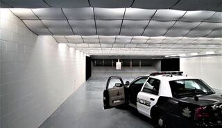 A police car is parked in a shooting range with an open door, under bright lights and a smooth, modern ceiling design.