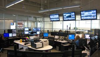 A modern control room filled with multiple computer stations, large screens displaying data, and staff actively monitoring information.