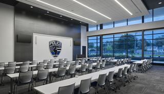 A modern training room featuring rows of chairs and tables, large windows, and a police department logo on the back wall.