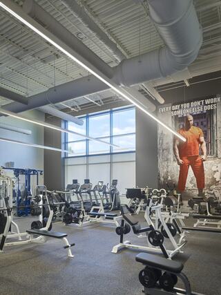 A well-equipped gym features various workout machines, large windows allowing natural light, and a motivational wall mural.