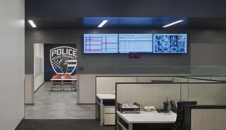 A modern police department office featuring workstations, digital displays, and a logo, with a hallway leading to meeting rooms.