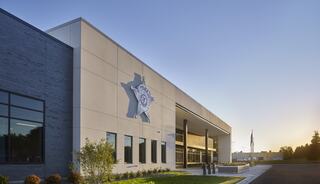 A modern law enforcement building features a large star emblem, large windows, and green landscaping, all under a clear blue sky.