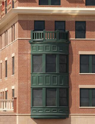 A green, bay-style window protrudes from a brick building, featuring decorative panels and a small balcony above.
