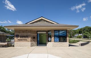 A modern building features large windows and a sign for Sunset Pool, surrounded by green trees and a clear blue sky.